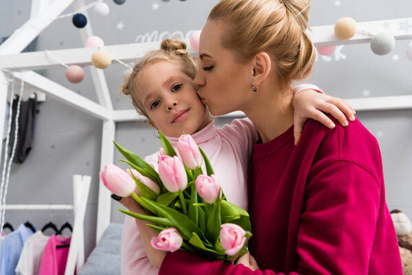 beautiful young mother with tulips bouquet kissing daughter