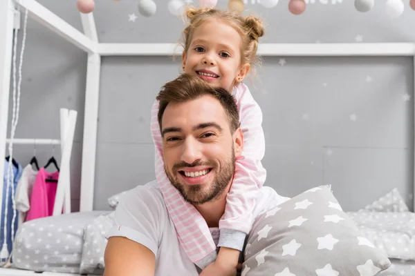 子供の寝室で父親を後ろから抱きしめる幸せの小さな娘 — ストック写真