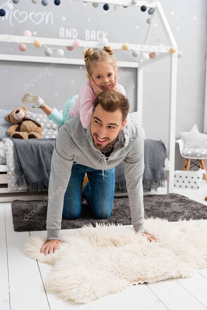 daughter riding on fathers back in kid bedroom