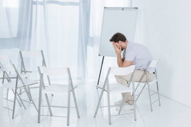 depressed middle aged man sitting on chair in empty room clipart