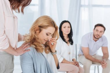 middle aged people supporting crying woman during anonymous group therapy  clipart