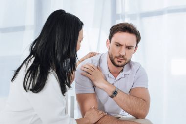 mature asian woman supporting upset man during group therapy clipart