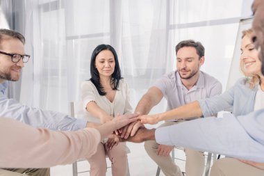 cropped shot of multiethnic middle aged people stacking hands during group therapy clipart