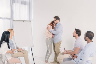 Boş beyaz tahta ve grup terapisi sırasında sandalyelere oturan diğer insanlar yakın dururken kaç sarılma Olgun  