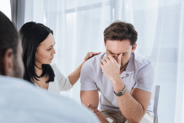 selective focus of mature asian woman supporting crying man during group therapy