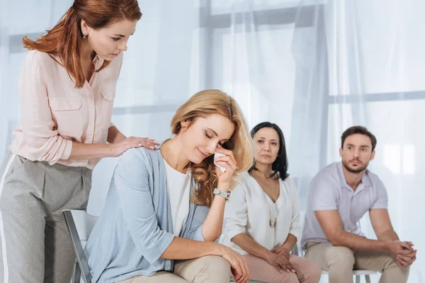 middle aged people supporting crying woman during anonymous group therapy