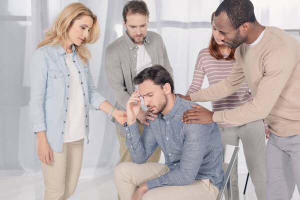 mid adult multiethnic people supporting upset man during group therapy  