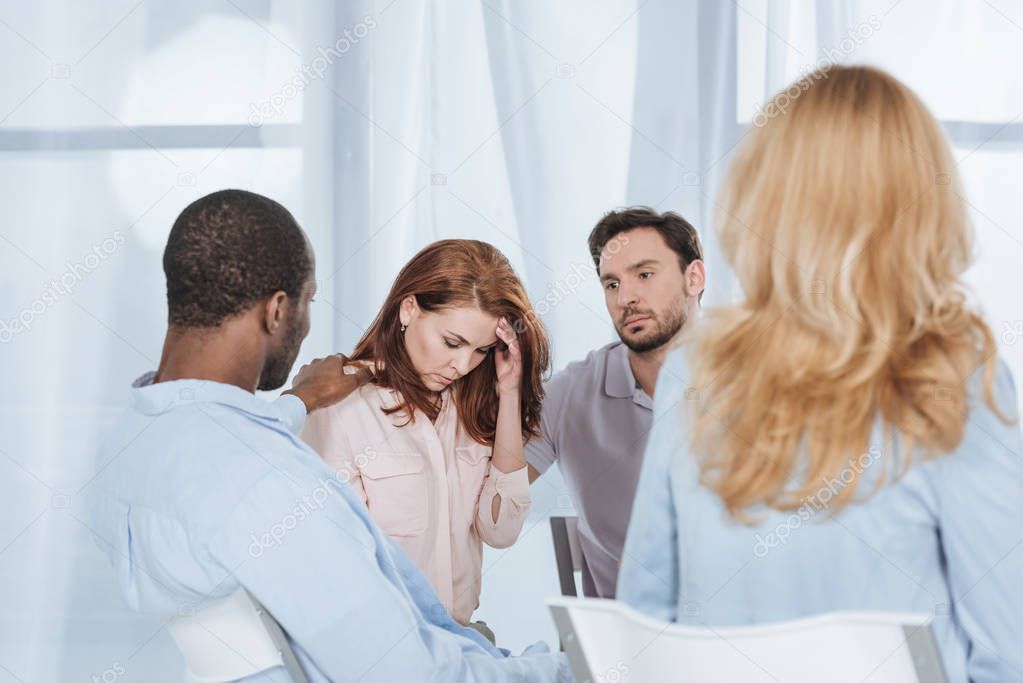 multiethnic middle aged people supporting depressed woman during anonymous group therapy