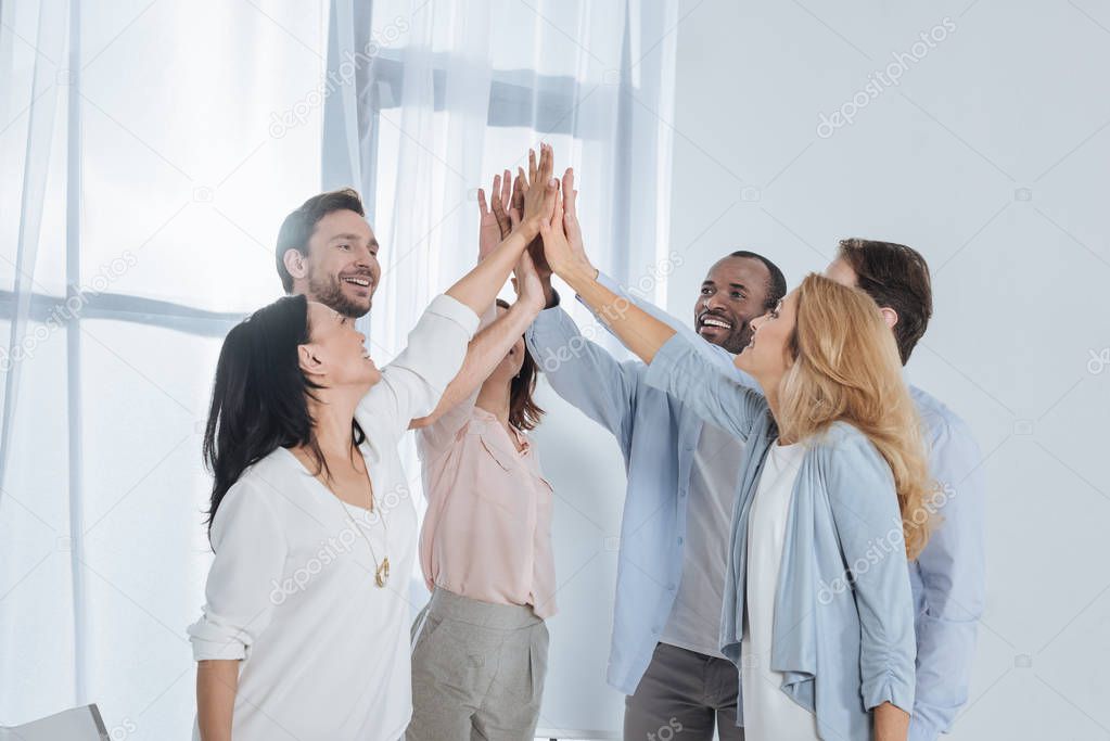 cheerful multiethnic mature people giving high five during group therapy
