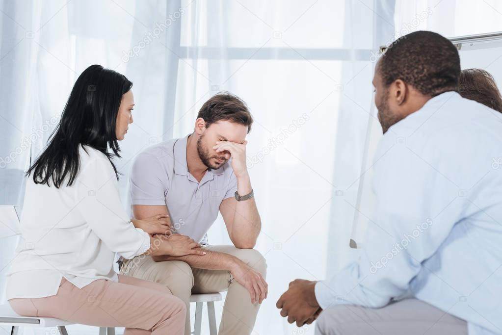 multiethnic mid adult people supporting depressed man during anonymous group therapy   