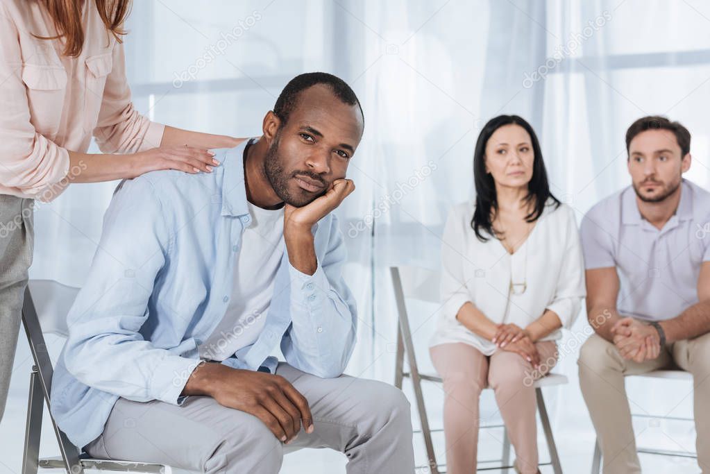 cropped shor of middle aged people supporting depressed african american man during anonymous group therapy