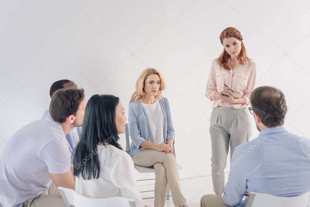 psychotherapist taking notes and working with mature multiethnic people during group therapy