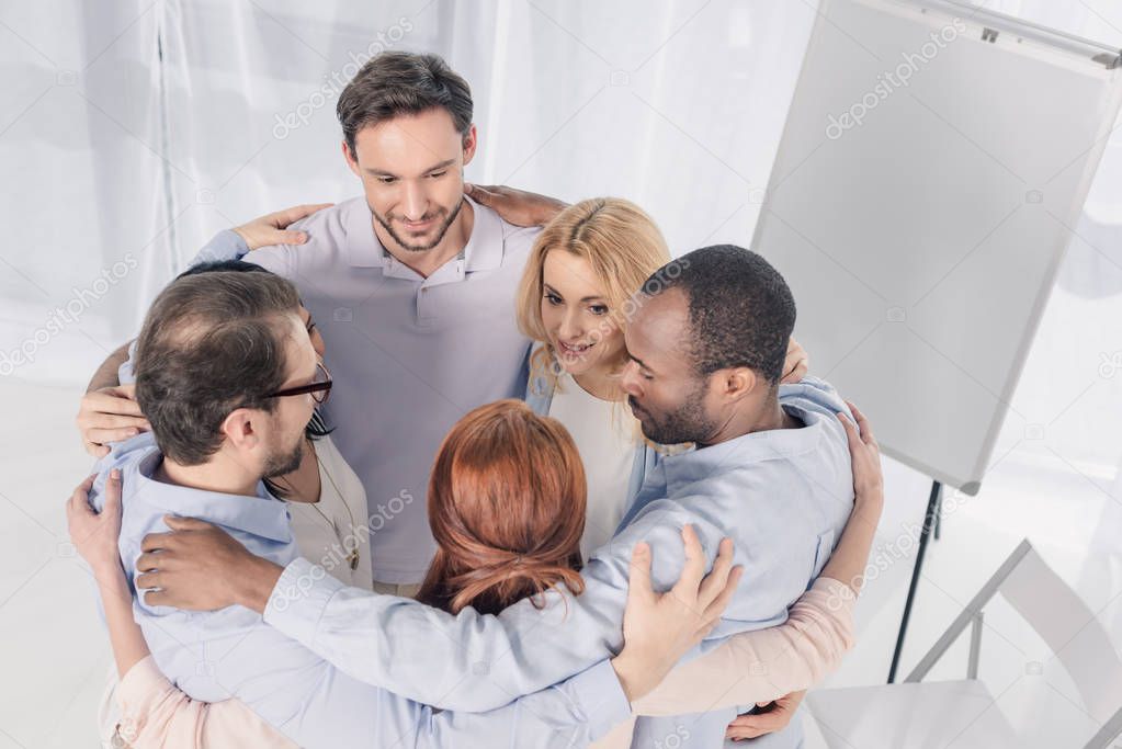 mature multiethnic people standing in circle and embracing during group therapy