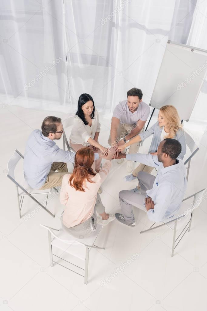 high angle view of multiethnic middle aged people sitting on chairs and stacking hands during group therapy