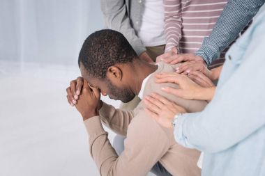 cropped shot of people supporting depressed african american man during group therapy