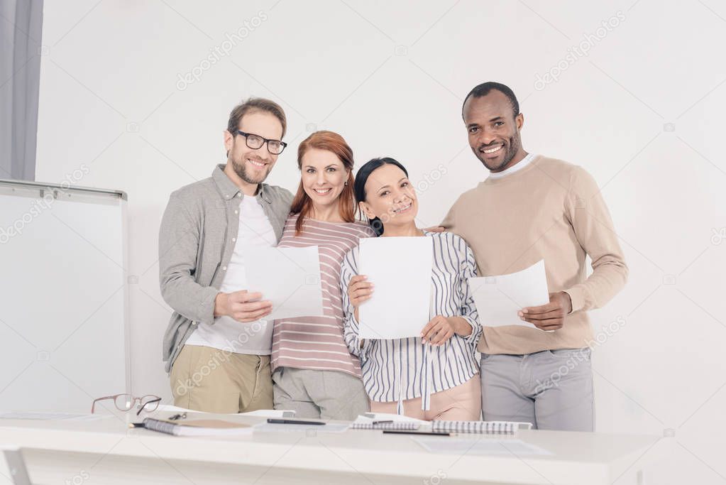 multiethnic middle aged people holding papers and smiling at camera