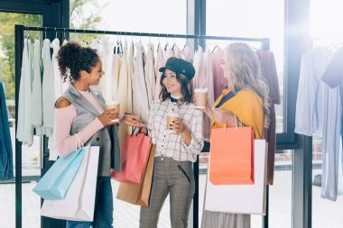 group of young women with shopping bags and coffee to go in clothing store