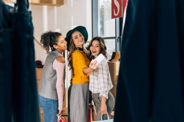 group of happy young women taking selfie in clothing store