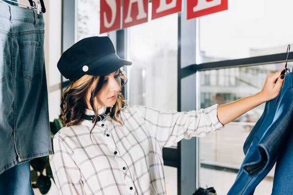 красивая молодая женщина смотрит на синие джинсовые платья в магазине одежды
