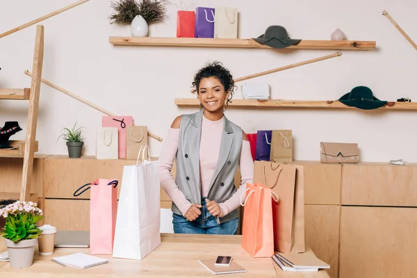 服装店经理站在工作场所与购物袋在桌上 — 图库照片