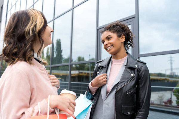 young stylish women with shopping bags and coffee to go talking outdoors