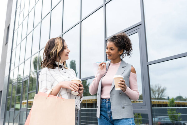young stylish women with shopping bags and coffee to go talking outdoors