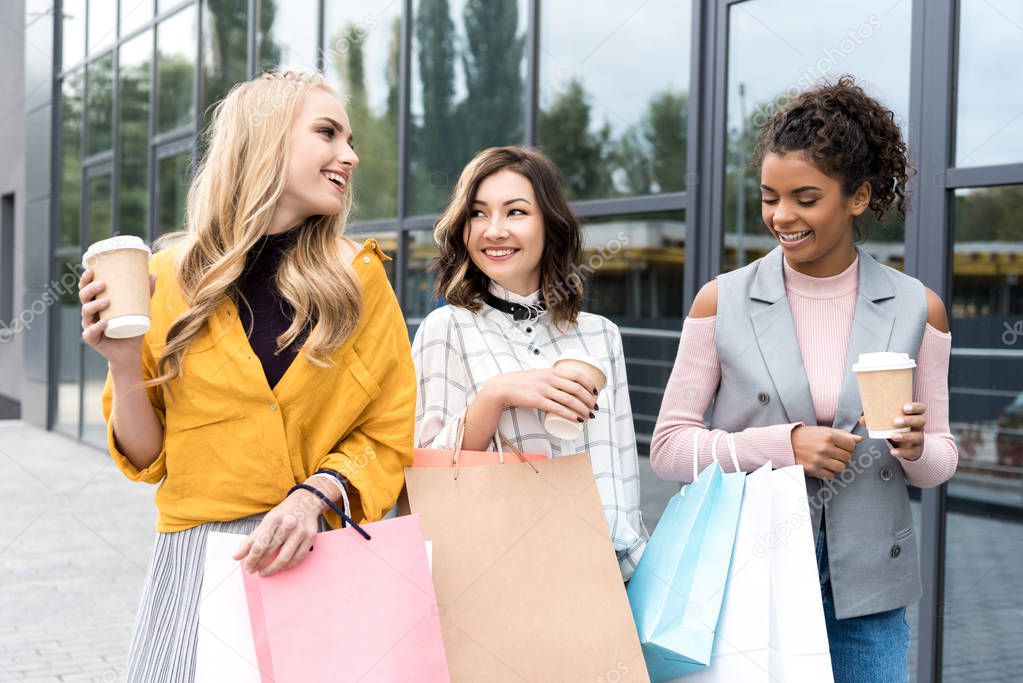 group of happy young women with shopping bags and coffee to go