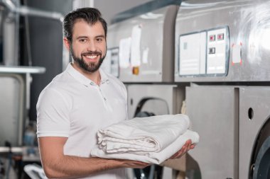 happy dry cleaning worker holding stack of clean clothes clipart
