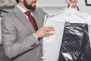 cropped shot of businessman holding plastic bag of clean clothing clipart