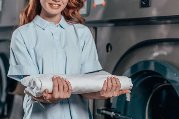 cropped shot of female dry cleaning worker holding stack of clean white clothes