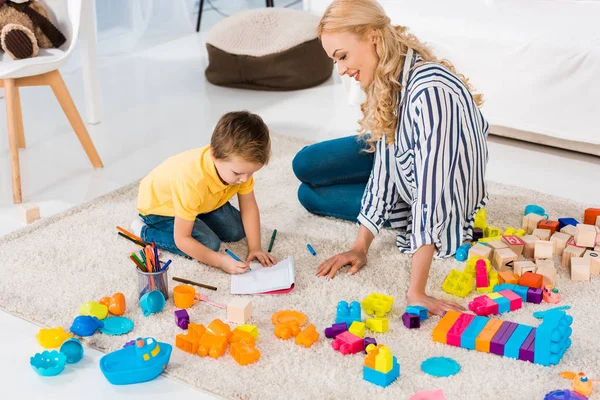 Giovane Madre Che Aiuta Figlio Mentre Disegna Insieme Casa — Foto Stock