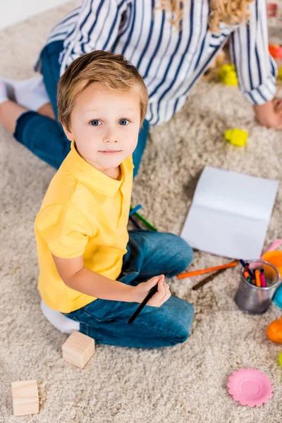 Enfoque Selectivo Niño Pequeño Mirando Cámara Mientras Dibuja Imagen Junto —  Fotos de Stock