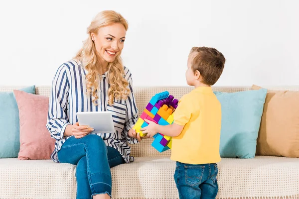 Niño Pequeño Mostrando Juguetes Madre Sonriente Con Tableta Sofá Casa — Foto de stock gratuita