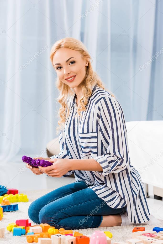 Side view of young mother with toys sitting on floor at home