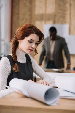 beautiful female architect discovering building plans while her colleague standing blurred on background clipart