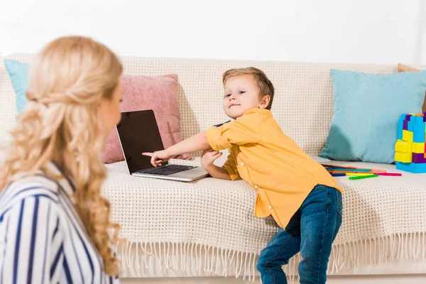Маленький Хлопчик Вказує Ноутбук Дивані Поки Мати Сидить Підлозі Вдома — Безкоштовне стокове фото