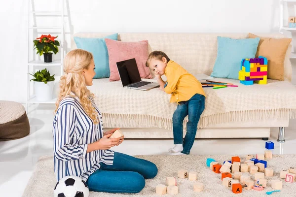 Little Boy Using Laptop Sofa While Mother Sitting Floor Home — Free Stock Photo