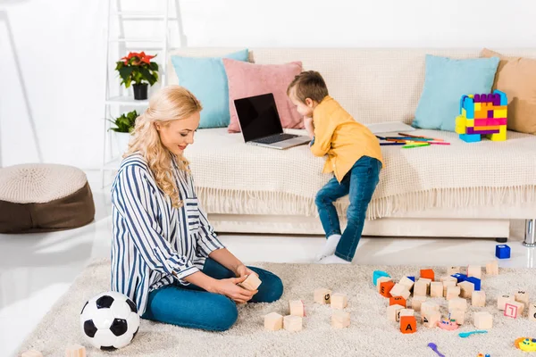 Little Boy Using Laptop Sofa While Mother Sitting Floor Home — Free Stock Photo