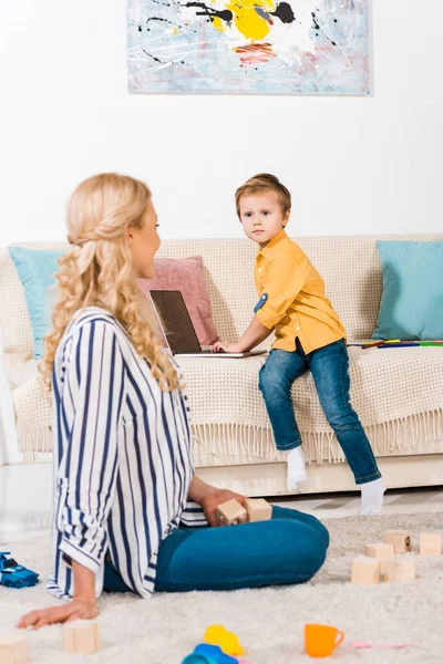 Little Boy Using Laptop Sofa While Mother Sitting Floor Home — Free Stock Photo