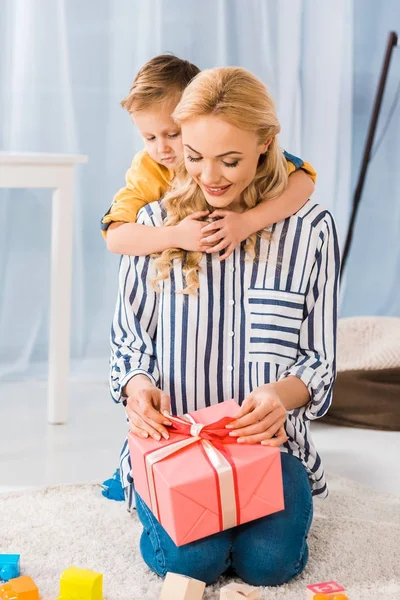 Piccolo Figlio Che Abbraccia Madre Con Regalo Avvolto Nelle Mani — Foto stock gratuita