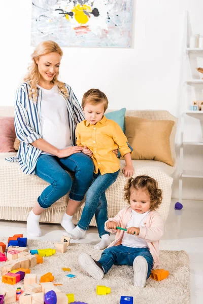 息子と遊ぶ娘のおもちゃを探して幸せな妊娠中の母親 — ストック写真