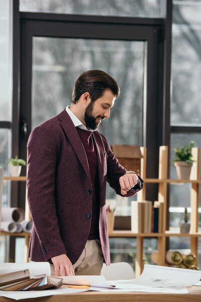 handsome architect looking at wristwatch in modern office