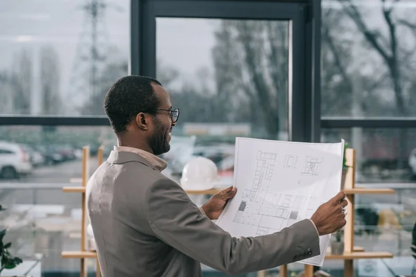 male african american architect looking at building plan in modern office