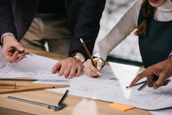 cropped view of multiethnic architects discussing and drawing building plans in office