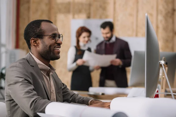 幸せなアフリカ系アメリカ人建築家の契約を議論する彼の同僚が近代的なオフィスでコンピューターでの作業 — ストック写真