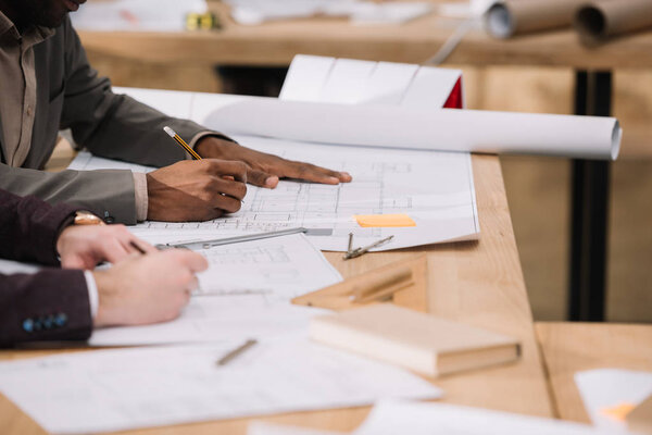 cropped shot of architects drawing building plans together at office