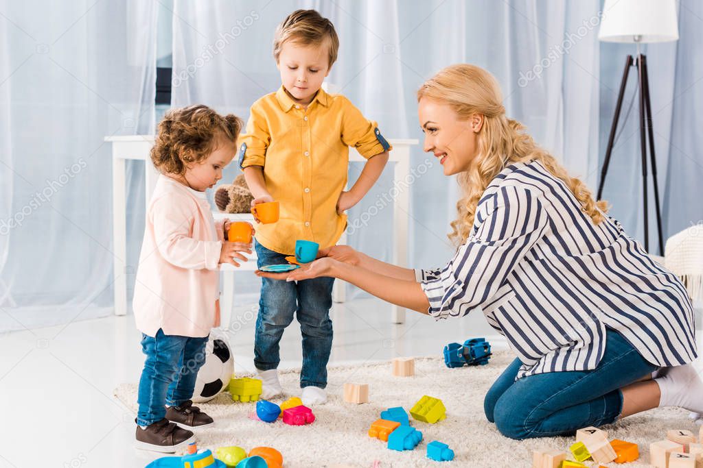 happy mother playing with son and daughter with plastic cups