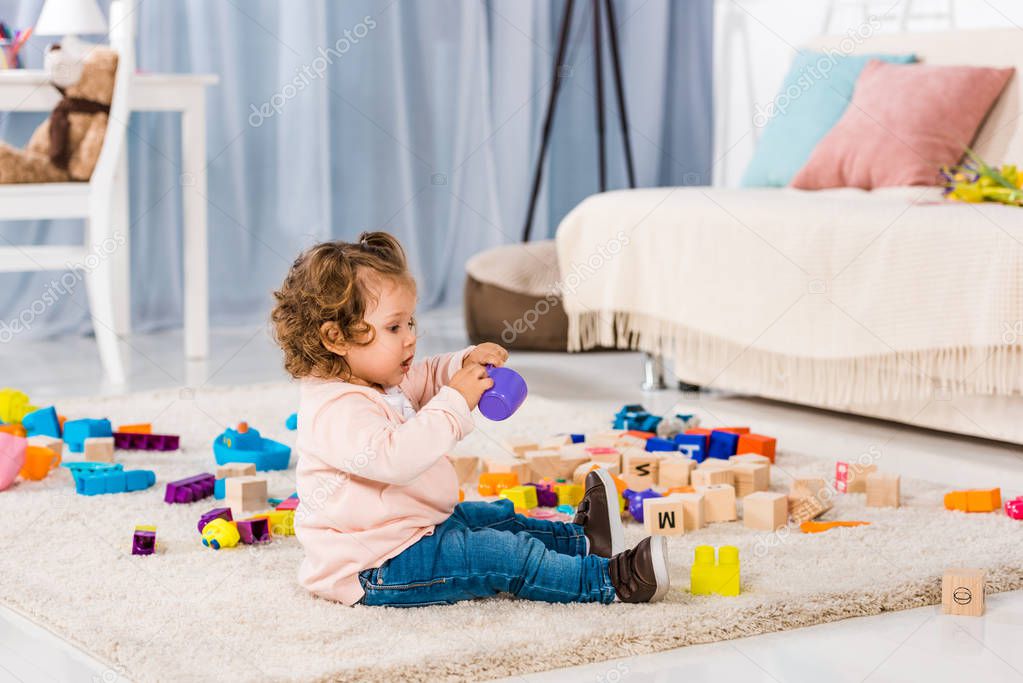 side view of adorable kid playing with plastic blocks on floor 