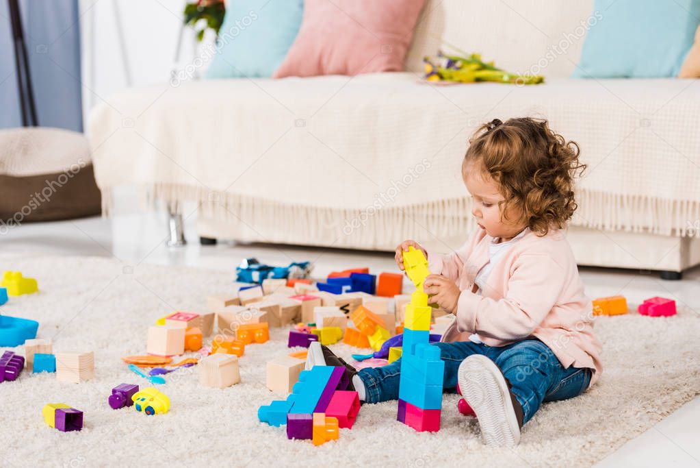 adorable kid playing with plastic blocks on floor  