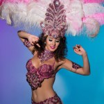 Happy young woman in carnival costume with pink feathers on blue background